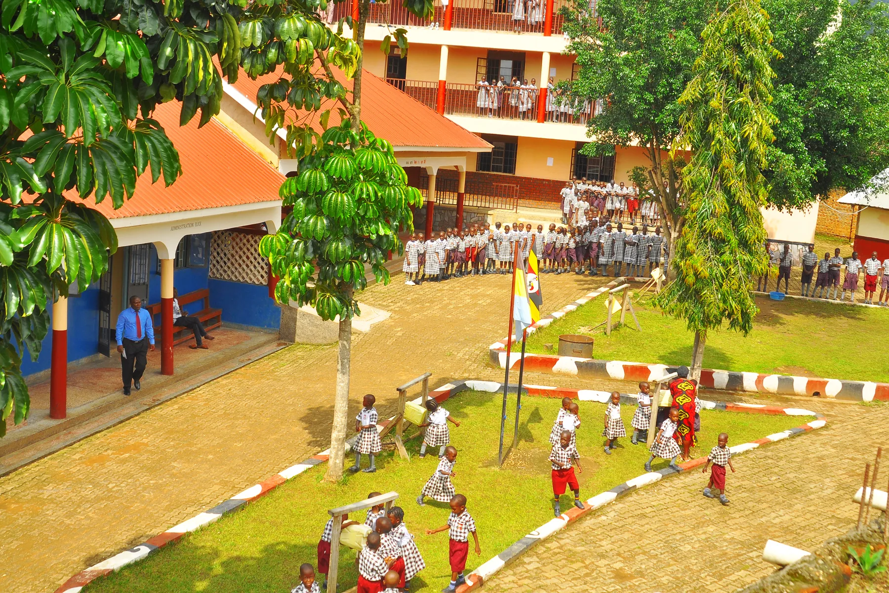 Children running in the courtyard beneath the trees and the school flag